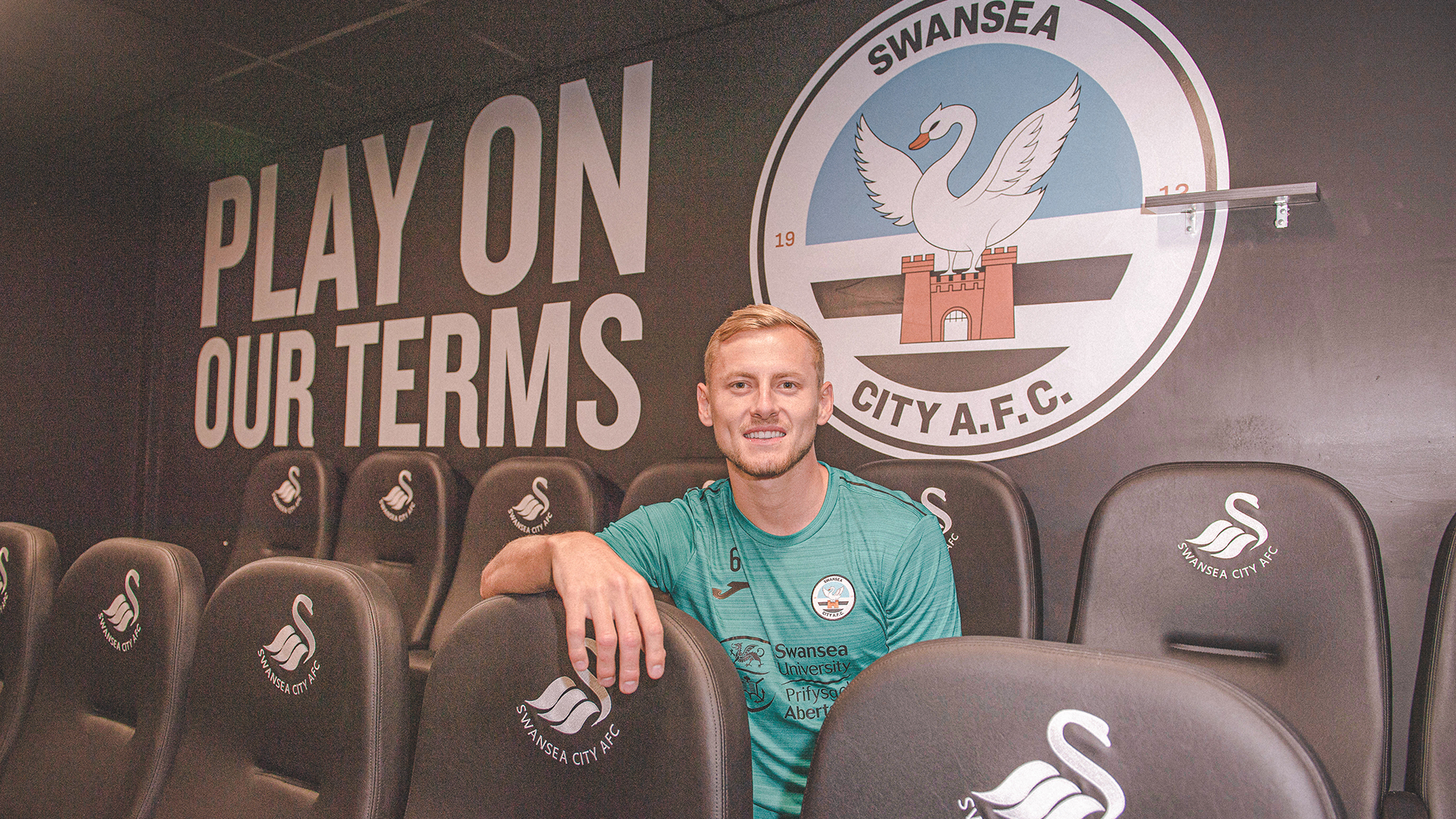 Harry Darling sat in front of the new Swansea City badge and the words play on our terms