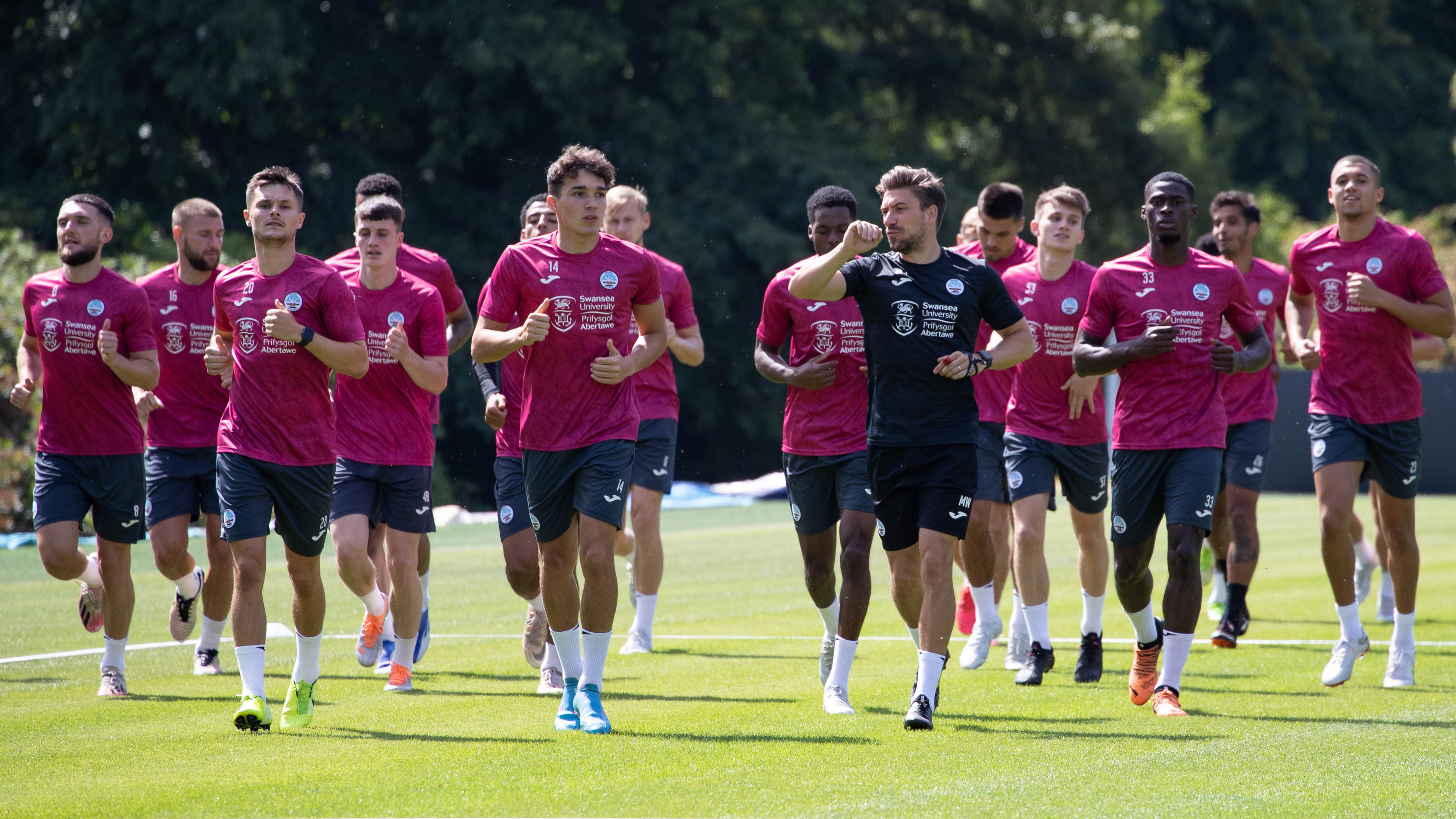 A group of Swansea City players wearing their training kit are jogging as a group