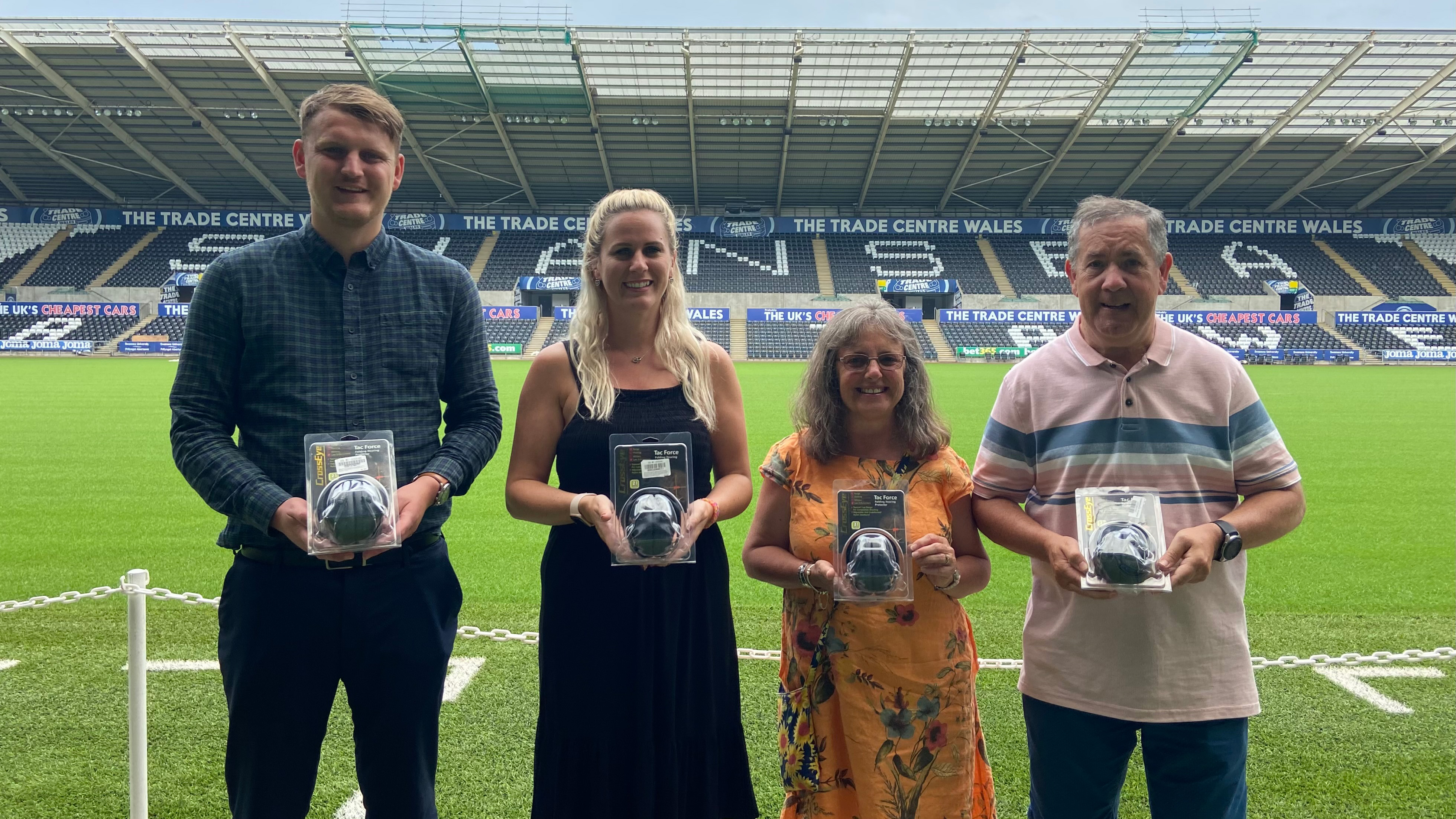 Two Swansea City staff and two members of the DSA holding brand-new ear defenders at pitch side