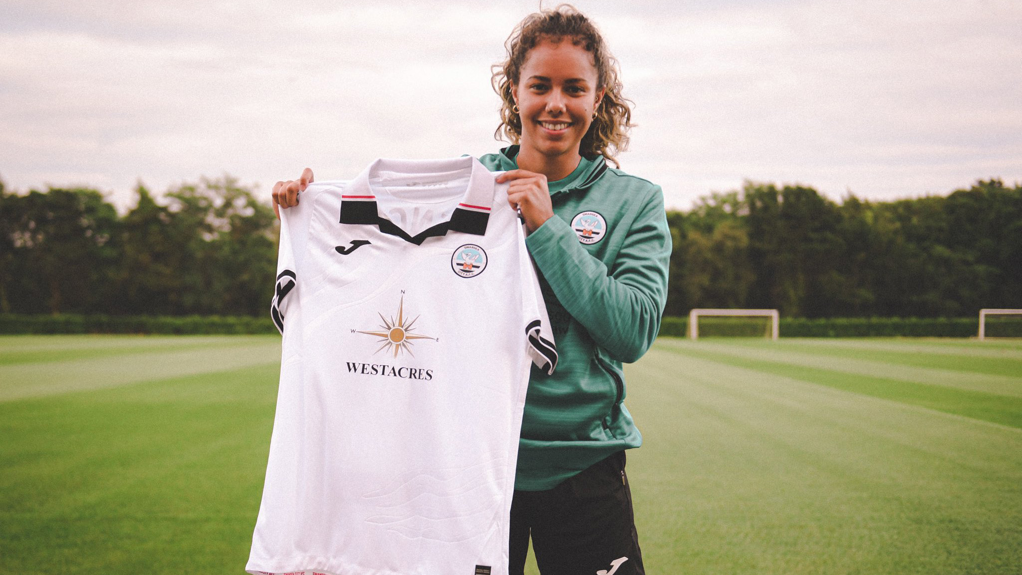 Monet Legall poses for a photo holding up a 2022-23 Swansea City shirt