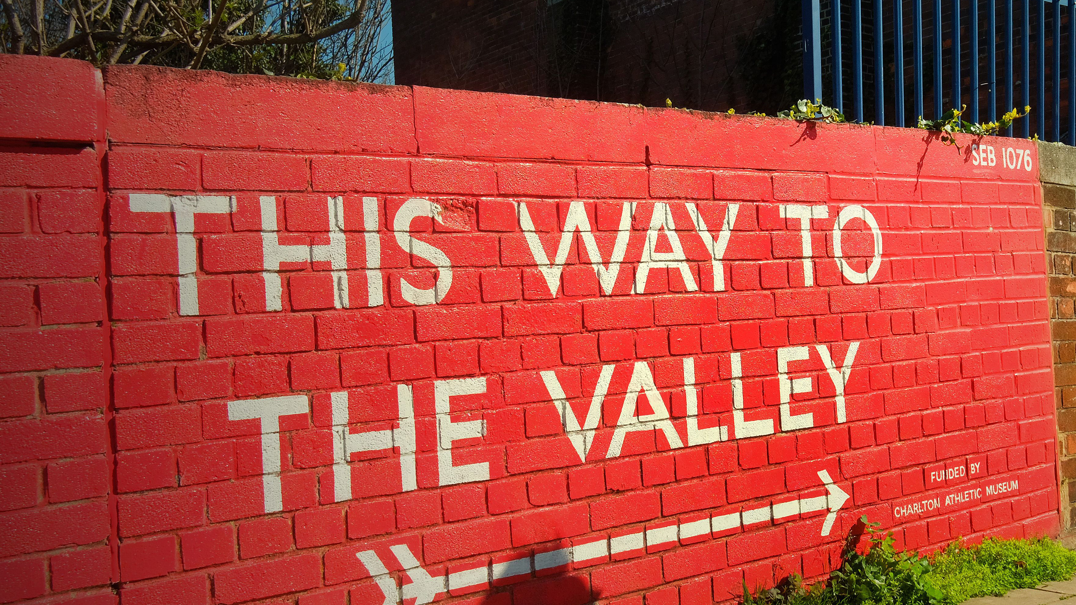 A wall painted red with the words "This way to The Valley" written on it.