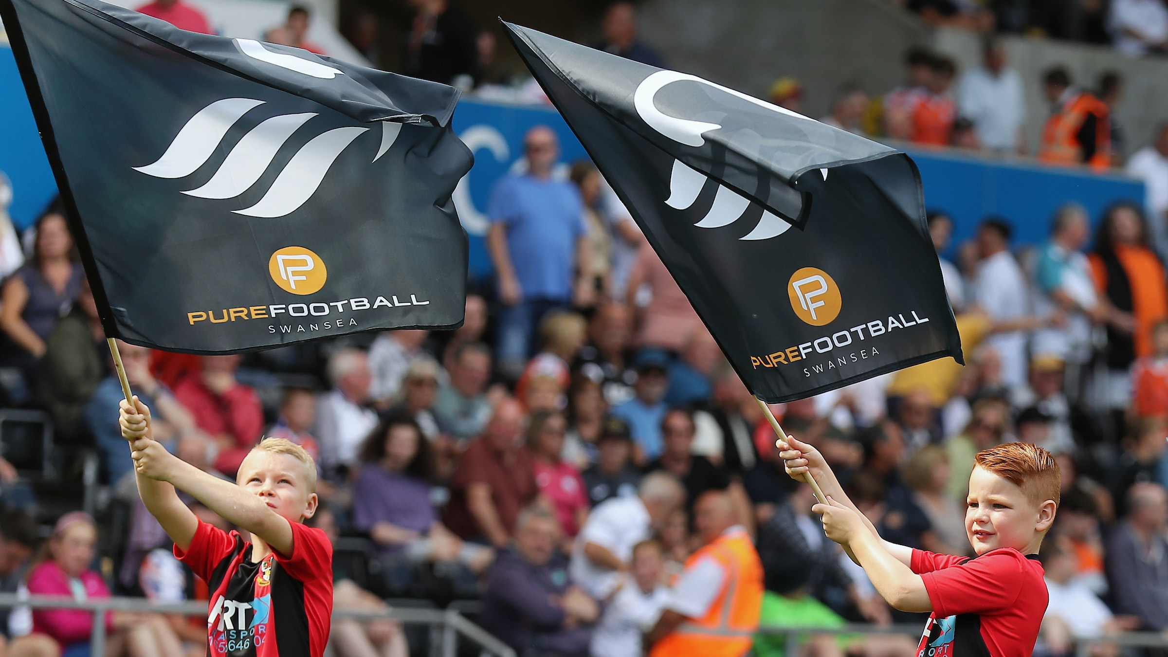 Two boys waving Swans flags with pure football logo