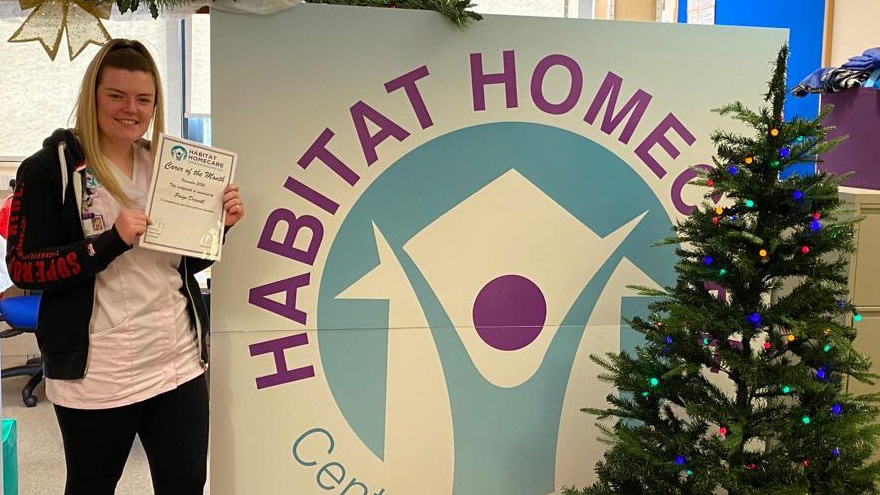The December Habitat Homecare winner poses in front of the charity logo and a Chirstmas tree 