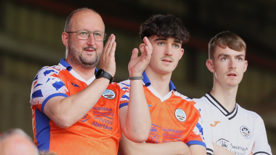 Three Swansea City fans watching the Charlton. One is clapping.